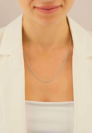 Collana con catena d'argento indossata da una persona con una maglietta bianca e un blazer. La collana presenta un design delicato con maglie sottili.