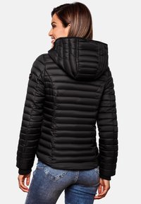 Zwarte pufferjack met horizontale stiksels, een vaste capuchon en elastische mouwen. Draagt met blauwe jeans, wat een aangesloten ontwerp laat zien.