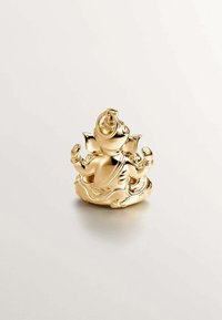 Estatua de color dorado de una figura sentada con orejas grandes, sosteniendo objetos en ambas manos, detallada con patrones en espiral y una base decorativa.