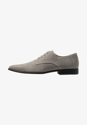 Gray suede dress shoe with a pointed toe, six lace eyelets, and a low black heel. Smooth texture with minimal stitching detail.