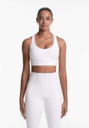 White sports bra with a scooped neckline and wide straps, paired with high-waisted white leggings featuring curved seams and a smooth texture.