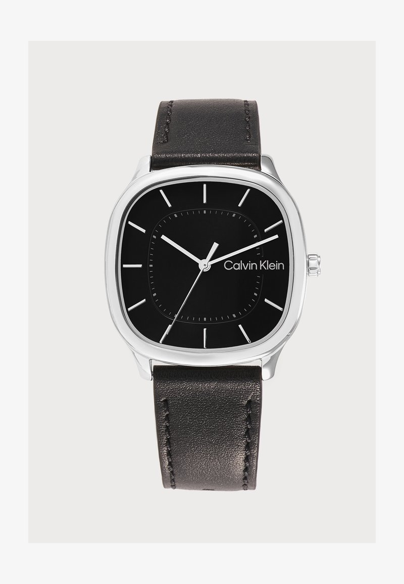 Montre-bracelet noire Calvin Klein avec boîtier carré argenté, index blancs simples et bracelet en cuir noir, affichant l’heure 10h10.