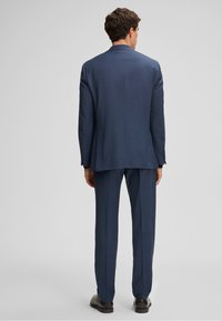 Marineblauer Anzug mit strukturiertem Stoff, strukturiertem Design und taillierter Passform. Die Rückseite zeigt einen Schlitz und elegante Hosen.