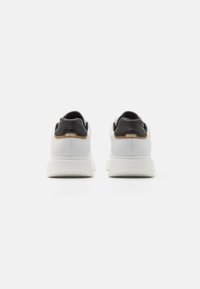 Ein Paar weiße Sneaker mit schwarzen Fersenkragen und brauner Verzierung, von hinten betrachtet, mit "BOSS"-Branding an jeder Ferse.