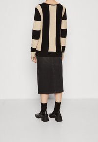 Czarny i beżowy sweter w paski z prążkowanymi mankietami, zestawiony z ciemnoniebieską spódnicą midi z denimu. Uzupełniony czarnymi butami na blokowym obcasie oraz prążkowanymi skarpetkami.