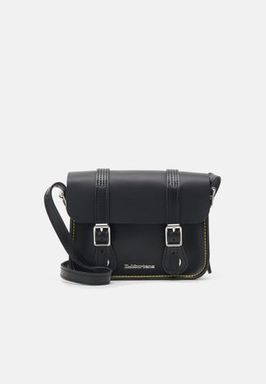 Bolsa de ombro preta em couro com aba, dois fechos prateados, costura amarela e uma alça ajustável. Apresenta uma textura suave e um design compacto.