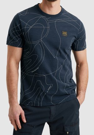 Camiseta de algodón azul marino con un patrón de líneas de contorno en blanco. Cuenta con un pequeño parche de logo rectangular en el pecho y un cuello redondo.