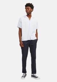Chemise à manches courtes bleu clair avec un bouton sur le devant, associée à un pantalon marine et des baskets. Tissu lisse et coupe décontractée.