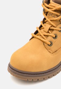 Botín de tobillo con cordones en material sintético amarillo, con puntera redondeada, cuello acolchado y suela texturizada con relieves profundos para tracción.