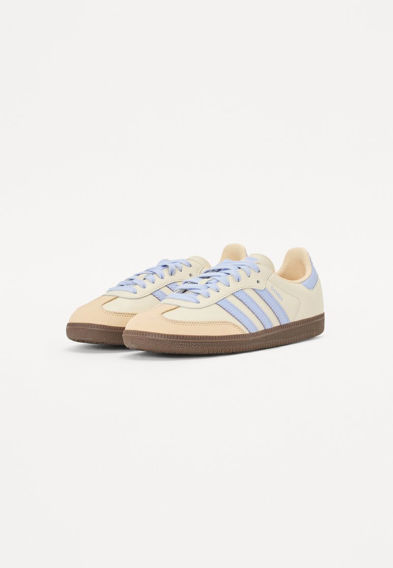 Beige en lichtblauwe sportschoenen met drie strepen, leren bovenwerk, ronde neus, rubberen zool en vetersluiting.