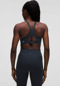 Mörkgrå sport-bh med racerback-design, som har en skärningsdetalj och justerbara axelband. De matchande leggingsen har en hög midja.