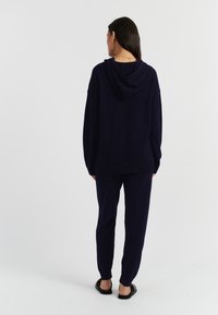 Felpa a maglia blu marina con vestibilità rilassata, dotata di cappuccio e polsini a costine. Abbinata a pantaloni tapered coordinati e sandali neri piatti.