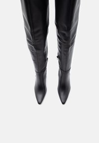 Botas negras por encima de la rodilla hechas de cuero suave, con punta afilada y un diseño ajustado y elegante con cremalleras laterales.