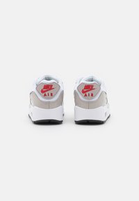 Nike Air-sneakers i vitt och beige, med mesh- och syntetmaterial, samt röda logotillbehör på hälen och svart gummisula.