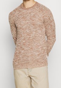 Texturerad stickad tröja i en varm brun nyans, med rundad hals och ribbade ärmslut. Tyget har ett prickigt mönster med ljusa inslag.