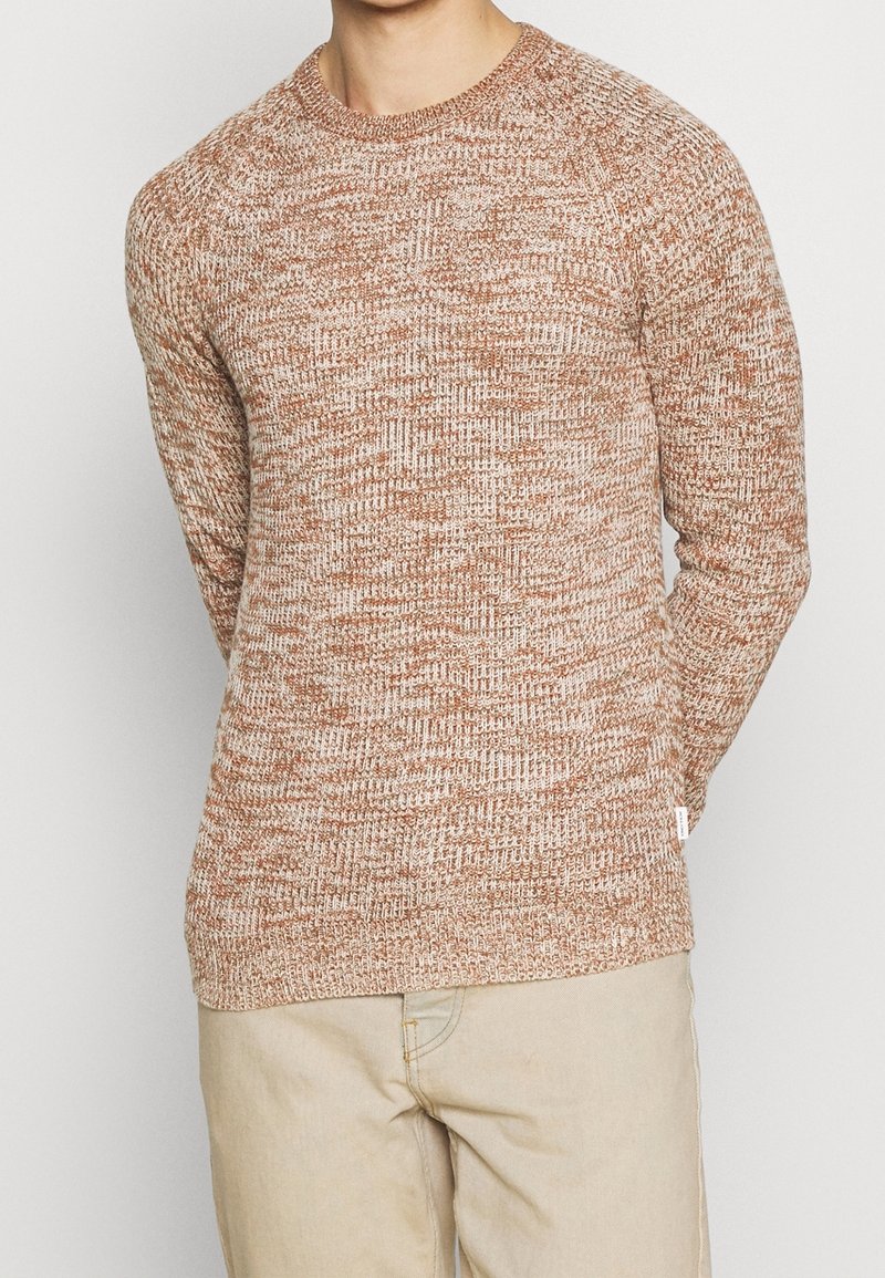 Texturerad stickad tröja i en varm brun nyans, med rundad hals och ribbade ärmslut. Tyget har ett prickigt mönster med ljusa inslag.