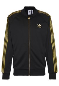 Svart zip-up jacka med guld tre-stripes design på ärmarna, ribbade mudd och nederkant, samt en guld Adidas-logotyp på vänster bröst.