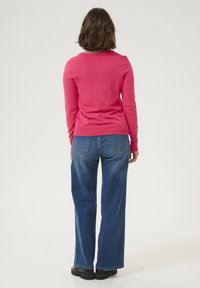 Pull en rose ajusté avec des manches longues, décolleté rond et texture lisse ; associé à un jean en denim bleu taille haute avec une coupe évasée.