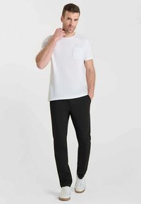 Wit katoenen T-shirt met een zakje, gecombineerd met een zwarte broek en witte sneakers. Zachte stof, comfortabele pasvorm en minimalistisch ontwerp.