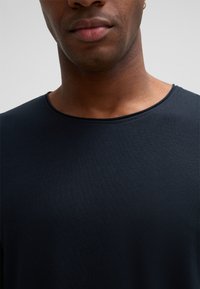 Schwarzes, geripptes T-Shirt mit rundem Halsausschnitt und weicher Textur, das eine Nahaufnahme des Brust- und Halsbereichs zeigt.