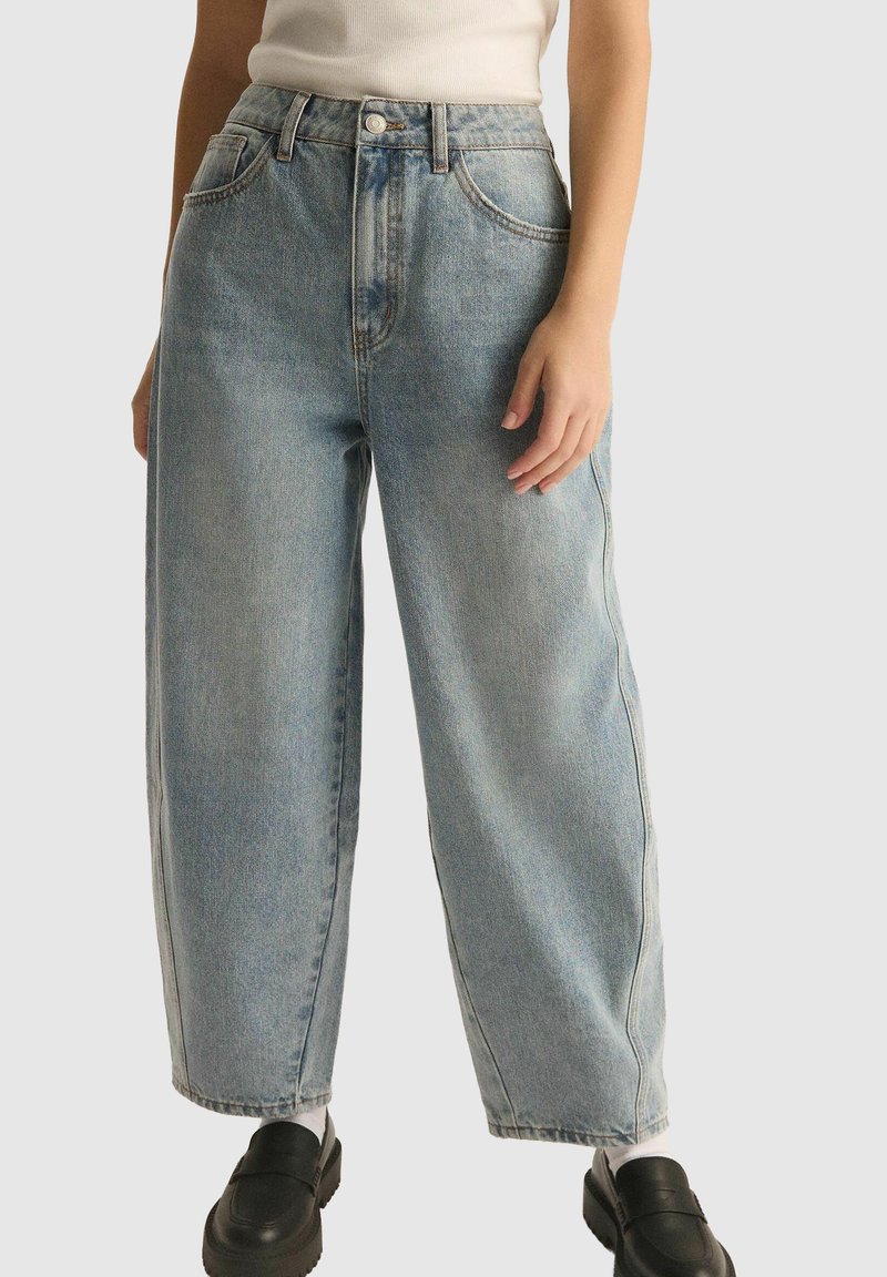 Jasnoniebieskie dżinsy o szerokich nogawkach z wysokim stanem, posiadające przednie kieszenie i wyblakłą teksturę. Wyposażone w zapięcie na guziki i przeszycia.