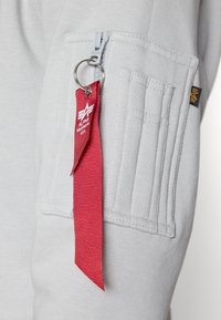 Felpa grigia con tasca con zip, coste testurizzate e un'etichetta in tessuto rossa. Include un attacco per portachiavi e dettagli del logo.