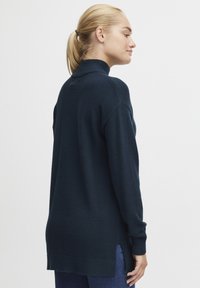 Marineblauer Pullover mit hohem Kragen, langen Ärmeln, seitlichen Schlitzen und einer weichen Textur; fällt unter die Hüften und hat gerippte Bündchen und Saum.