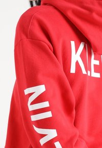 Felpa con cappuccio rossa con una grande scritta grafica bianca "KLE" sul davanti e "NI" lungo la manica sinistra. Realizzata in tessuto morbido e strutturato.