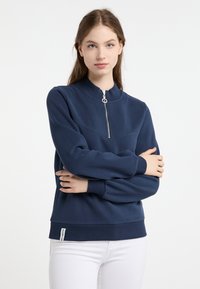 Felpa blu navy con colletto alto, zip frontale a metà, polsini e orlo a coste. Tessuto morbido e testurizzato; piccola etichetta nell'angolo in basso a sinistra.