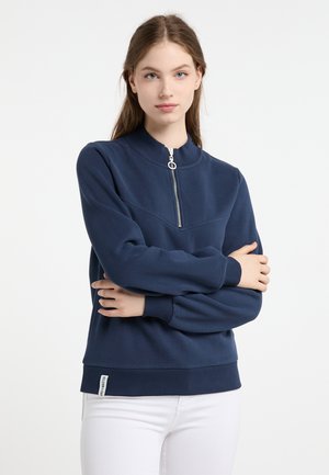 Felpa blu navy con colletto alto, zip frontale a metà, polsini e orlo a coste. Tessuto morbido e testurizzato; piccola etichetta nell'angolo in basso a sinistra.