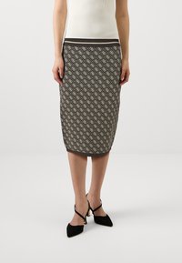 Jupe crayon tricotée en marron foncé avec un motif géométrique crème, présentant une silhouette ajustée et une taille contrastante. Talons noirs visibles.