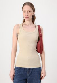 Beige ribbatoppi, jossa on pyöreä pääntie, yhdistettynä tiukkoihin tummansinisiin farkkuihin ja pieneen punaiseen olkalaukkuun.
