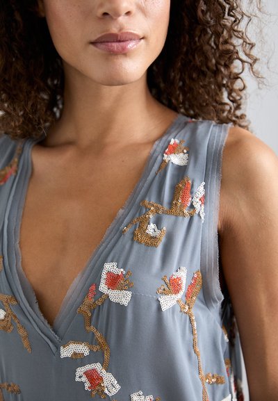 Hallitus hall vest, millel on sügav V-kaelus, mis on kaunistatud lillemotiividega valges, oranžis ja kuldsetes sädelevates detailides kerge ja läbipaistva kangaga.