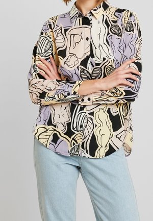 Chemise à manches longues boutonnée avec figure nue abstraite et motifs de feuilles en violet pastel, beige, noir, associée à un jean bleu clair.