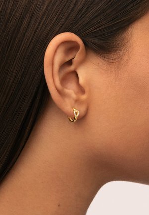 Aro de oro con una gema transparente en forma de corazón en la parte frontal, que presenta una textura suave y un diseño moderno y elegante.
