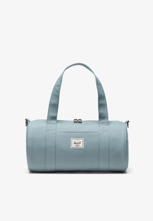 Bolsa de lona azul claro hecha de tela duradera, con dos asas resistentes, cierre de cremallera y un parche con logo en el frente.