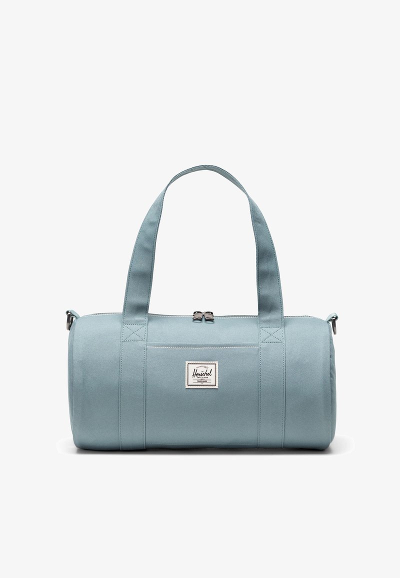 Svetlomodrá taška typu duffel vyrobená z odolnej látky, vybavená dvoma pevnými rukoväťami, zapínaním na zips a logovou nášivkou na prednej strane.