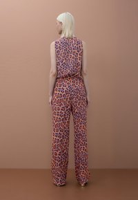 Mono con estampado de leopardo en tonos naranja, púrpura y negro, con diseño sin mangas y pantalones de pierna ancha. Textura de tela suave.