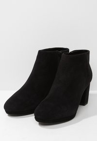 Botines de ante negros con punta redonda, cremallera lateral y tacón ancho. Textura suave con detalles de diseño minimalistas.