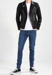 Svart lädermotorcykeljacka med silverdragkedjor, parat med en vit t-shirt, blå jeans och svarta sneakers. Enkel, figurnära design.