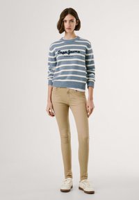 Prugasta pletena pulover v svetlo modri in kremni barvi, z vezenim logotipom. Prikladne bež hlače in bele superge dopolnjujejo obleko.