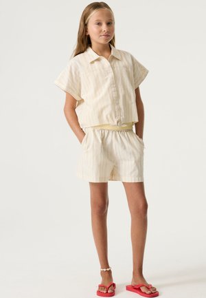 Camicia a righe beige in cotone a maniche corte con bottoni, abbinata a pantaloncini coordinati e fascia in vita gialla. Indossata con infradito rosa.