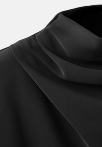 Top de tela negra con escote drapeado y textura suave, con un diseño fluido y suave que resalta los pliegues y contornos delicados.