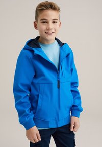 Modra zip-up jakna s kapuco, izdelana iz gladkega materiala. Ima sprednje žepe in elastične manšete. Nošena preko svetlo modre srajce.