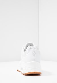 Weißer Sportschuh mit einer strukturierten Oberseite, die Perforationen aufweist, glattem Fersenbereich und einer neutralen Gummilaufsohle.