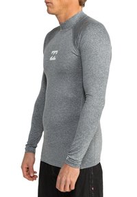 Rash guard de manga larga gris con cuello alto, fabricado en material elástico, con un logo de olas en el pecho y costuras reforzadas.