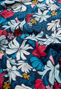 Tissu bleu marine à motif floral avec de grandes fleurs blanches, rouges, roses et bleues, entourées de feuilles vertes et jaunes. La texture semble douce.