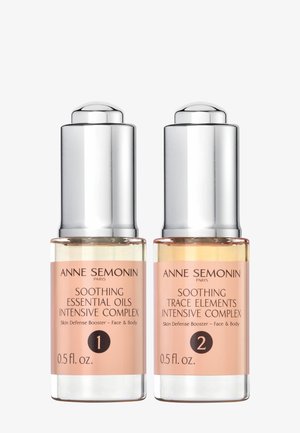 Deux flacons cosmétiques en verre avec des bouchons argentés, arborant des étiquettes roses. L'un est étiqueté « Huiles essentielles apaisantes » et l'autre « Éléments traces apaisants ». 