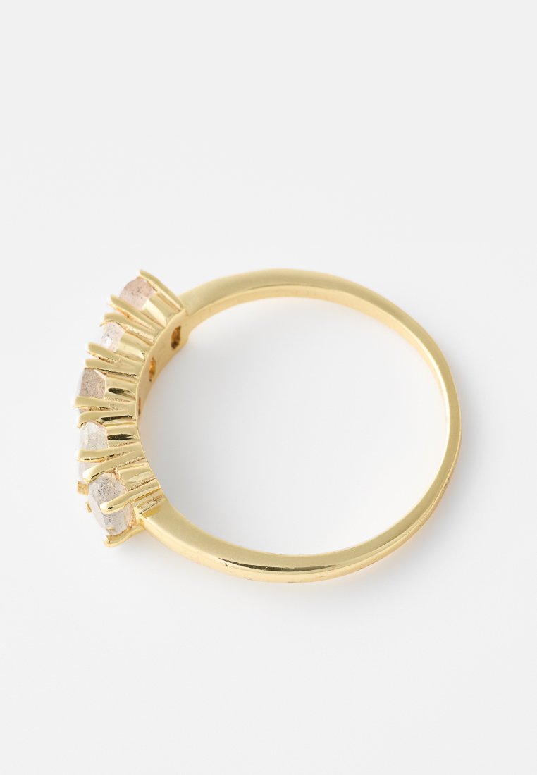 Gouden ring met vijf asymmetrische heldere stenen, geplaatst in een verhoogd ontwerp. Gladde afwerking met een gepolijste band, minimalistisch en modern.
