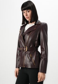 Burgundy leather jacket with a belted waist, gold hardware, asymmetrical zipper, and two zippered front pockets. Soft texture, tailored fit.